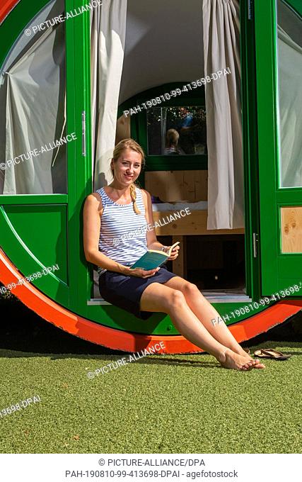 23 July 2019, Saxony, Königstein: A woman sits with a book in her hand on the threshold of the concrete tube hotel room in Königstein in Saxony