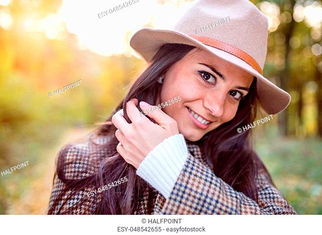 Beautiful young woman in checked coat and brown hat in autumn forest
