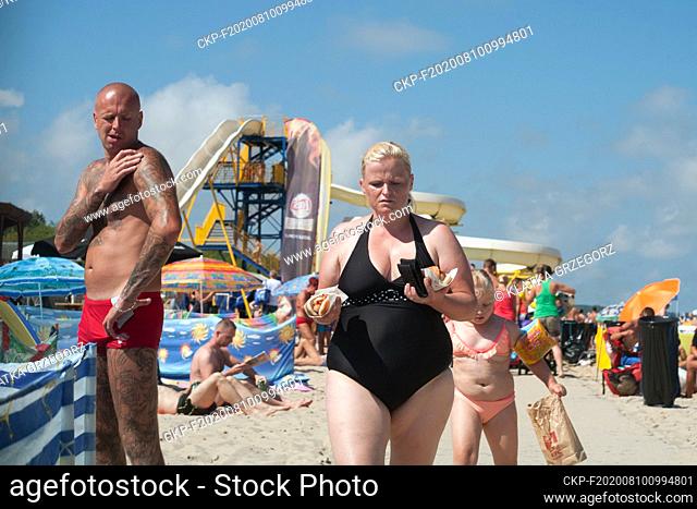 Poland, Beach in the Wladyslawowo in Pomeranian province 13.08.2015. Woman with girl holding hot dogs. Waterslide can be seen in the background