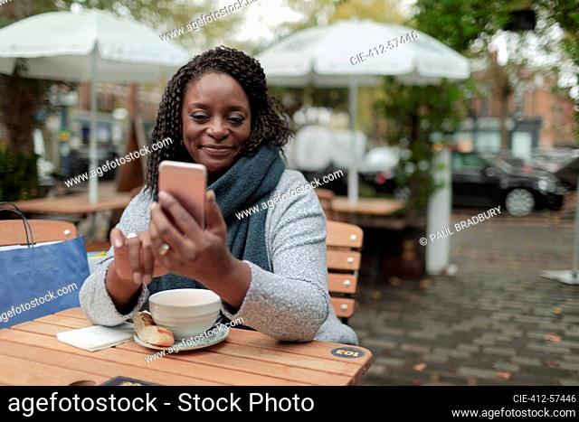 Happy woman with coffee using smart phone at table on cafe patio