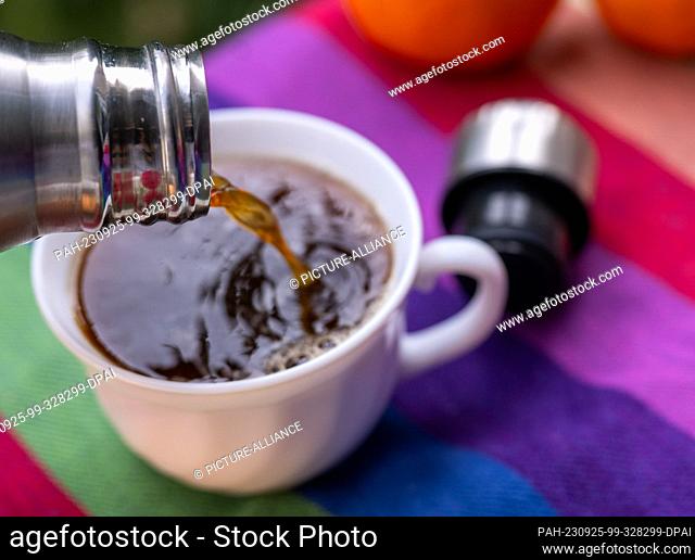 ILLUSTRATION - 17 September 2023, Berlin: Warm coffee flows from a thermos flask into a cup standing on a picnic blanket