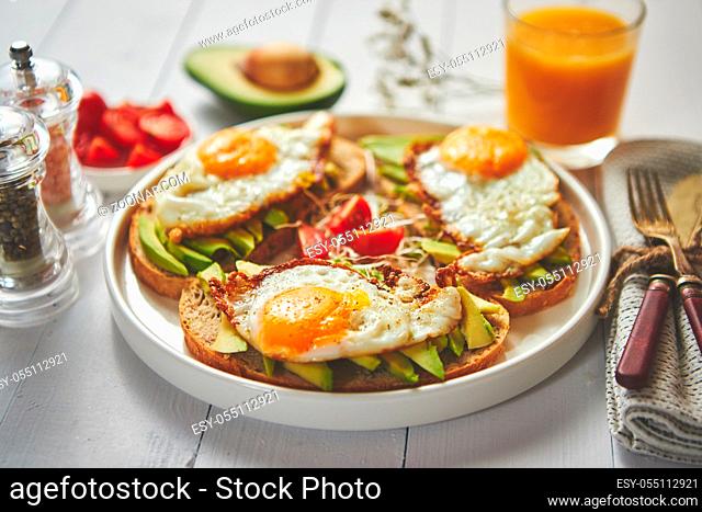 Delicious healthy breakfast with sliced avocado sandwiches with fried egg on top of bread. With orange juice, cherry tomatoes, radish sprouts, salt and peper