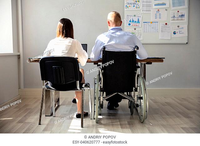 Rear View Of Disabled Businessman With His Colleague Working On Laptop