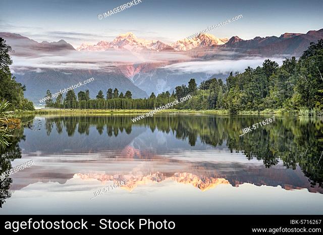 Veil clouds in front of Mount Cook and Mount Tasman are reflected in Lake Matheson in the evening light, Westland National Park, Fox Glacier, Whataroa