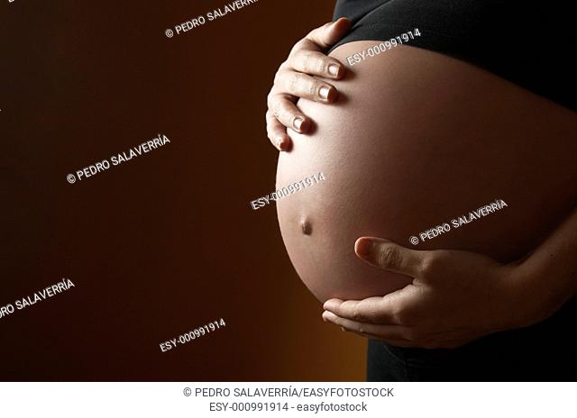 pregnant woman caressing her belly with orange background