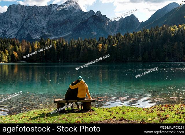 Rear view of couple sitting on bench at Laghi di Fusine, Friuli Venezia Giulia, Italy