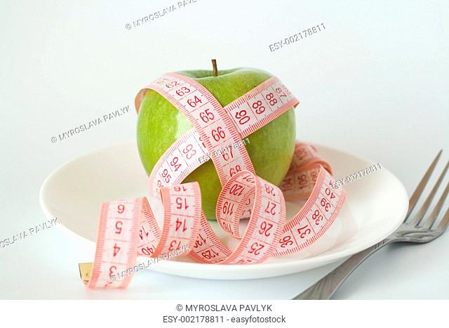 Green apple and measuring tape on a white plate and fork