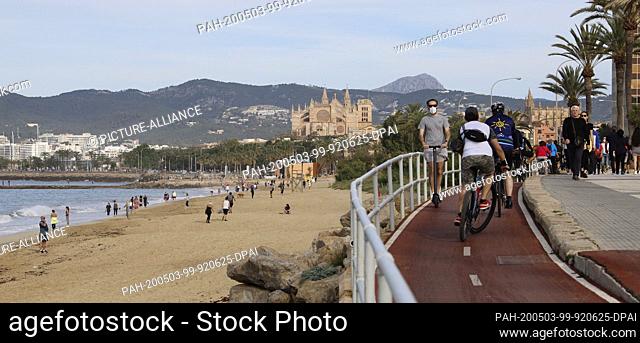 02 May 2020, Spain, Palma: People cycle and walk above the beach ""Can Pere Antoni"", in the middle of the picture there is the cathedral of Saint Mary