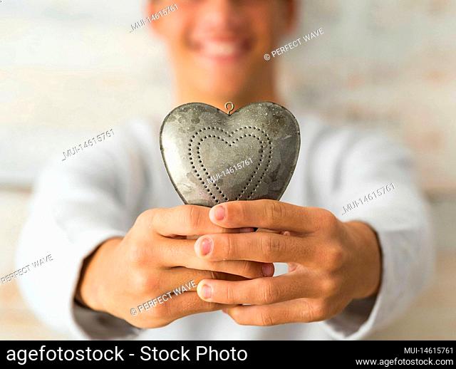 close up of hands of teenager or man holding in his hands a metal heart smiling - love and passionate lifestyle