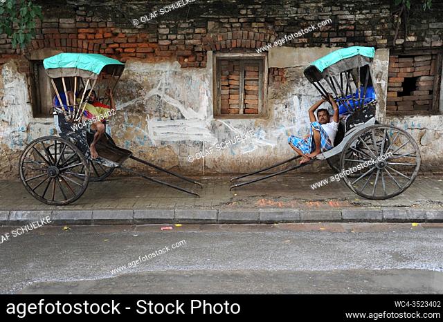 Kolkata (Calcutta), West Bengal, India, Asia - Two rickshaw pullers rest on their traditional old style wooden rickshaws at the roadside in the Indian...