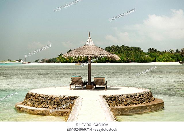 travel, tourism, vacation and summer holidays concept - palapa and sunbeds over sea and sky on maldives beach