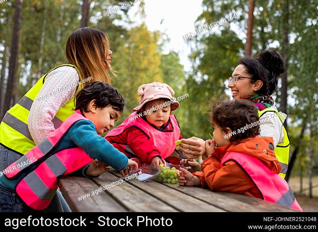 Preschool teachers and students eating grapes outdoors