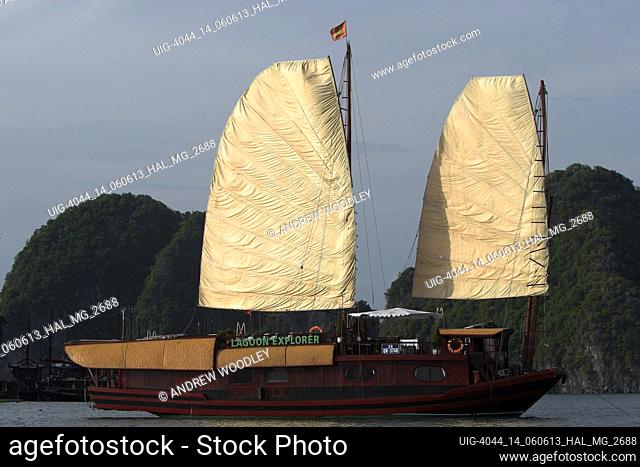 Eighty foot motorized junk cruiser with sails hoisted among the rocky islands of Halong Bay Vietnam