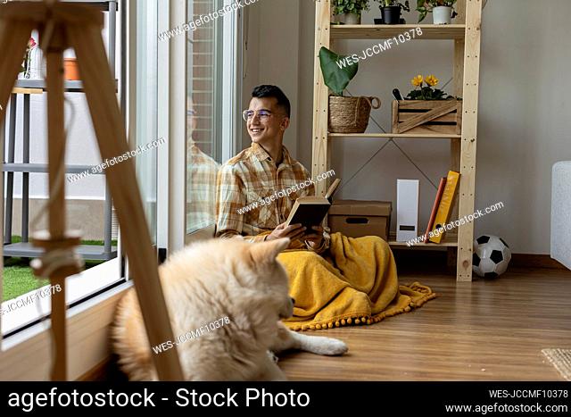 Smiling man holding book looking out of window at home
