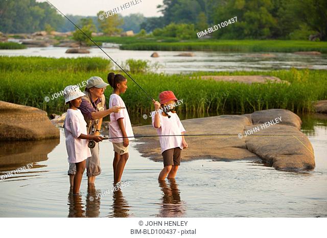 Woman teaching children how to fly fish on river