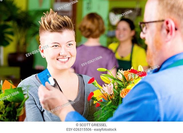 Young smiling customer watching floral shop clerk swipe credit card on tablet computer