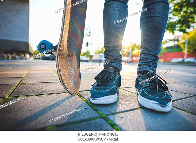 Legs and feet of young male urban skateboarder standing on sidewalk