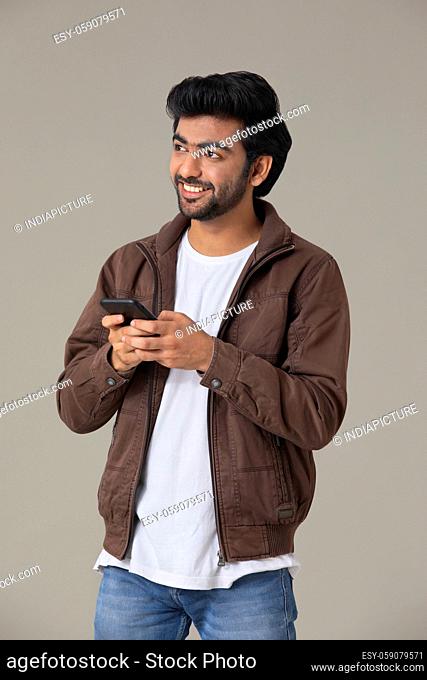 A YOUNG MAN LOOKING ABOVE WHILE USING MOBILE PHONE