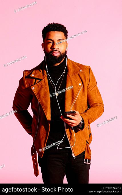 Cool African American man with beard, listening music, looking at camera, isolated on pink studio background