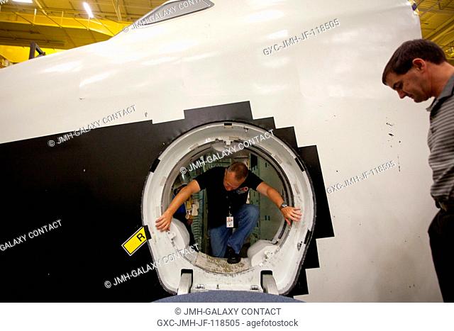 NASA astronaut Doug Hurley crawls out of the Crew Compartment Trainer (CCT-2) mock-up while Rex Walheim waits as the crew of STS-135 trains in the Space Vehicle...