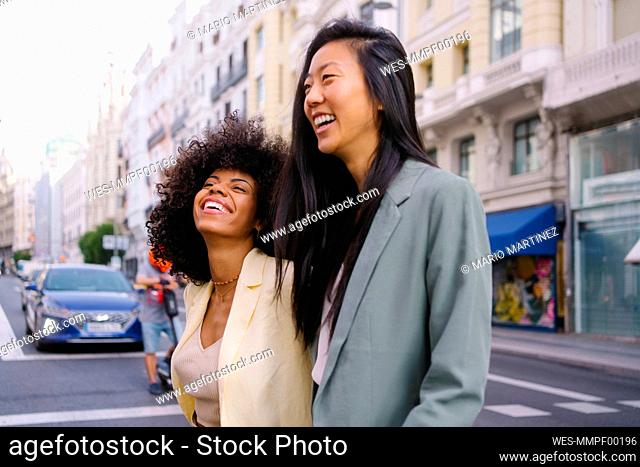 Cheerful multiracial friends crossing road in city