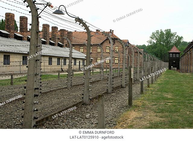 Barbed wire fence with concrete posts and search lights enclosing brick built blocks in the compound of Auschwitz 1 concentration camp with a black wood guards...