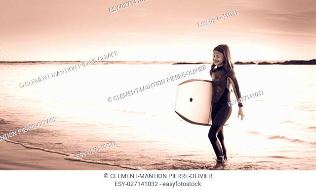 girl with bodyboard, dressed with a wetsuit walking on the beach in the direction of the ocean