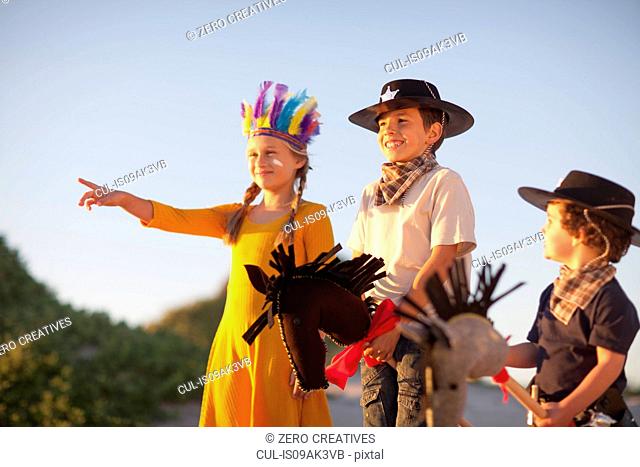 Three children dressed as native american and cowboys pointing from sand dunes