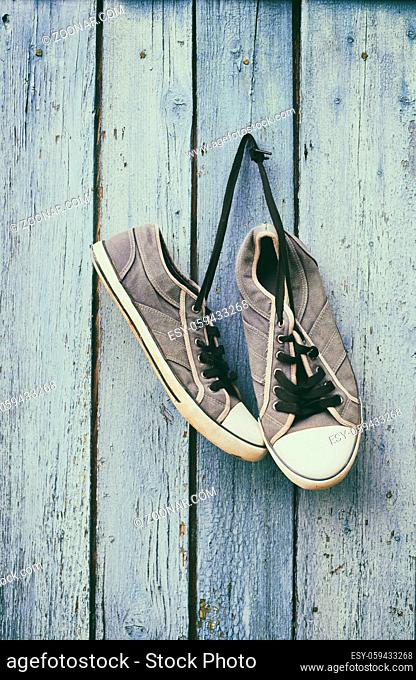 old male blue sneakers hang on a nail on a blue wooden wall, vintage toning
