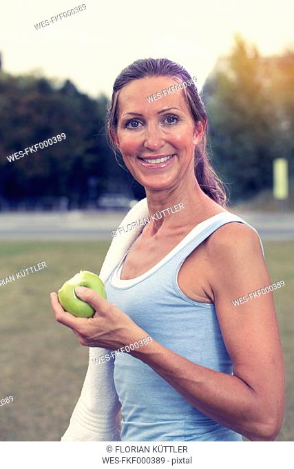 Sportive mature woman with towel around her neck holding apple