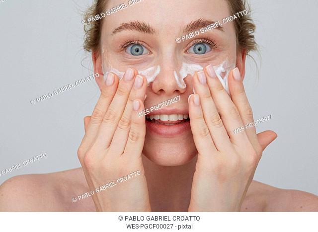 Portrait of blond young woman applying cream on her face