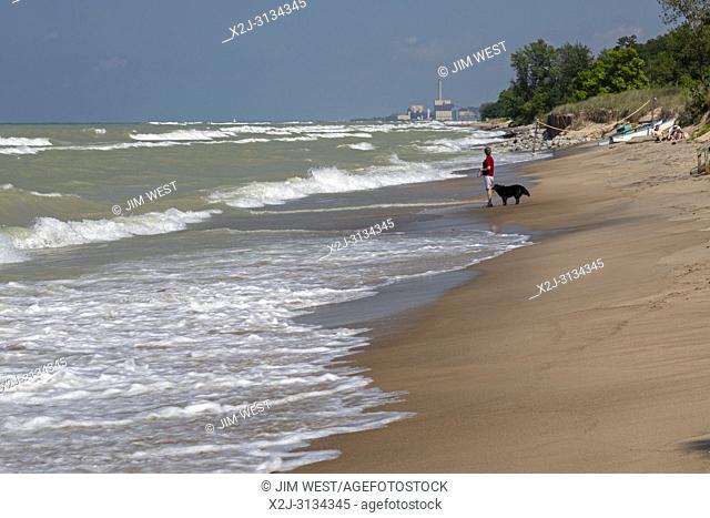 Beverly Shores, Indiana - A woman walks her dog on the beach of Indiana Dunes National Lakeshore, at the southern end of Lake Michigan