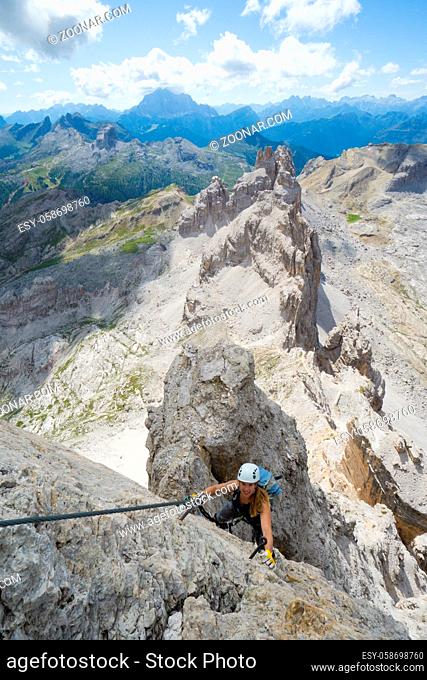 Vertical view of an attractive female climber on a steep Via Ferrata in the Italian Dolomites with a great view behind
