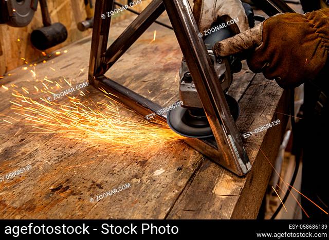 A closeup view of hot sparks flying from the abrasive disc of an angle grinder whilst a blacksmith polishes a metal frame