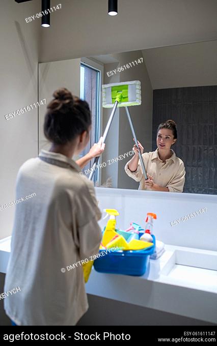 House work. Young woman cleaning mirror in the bathroom