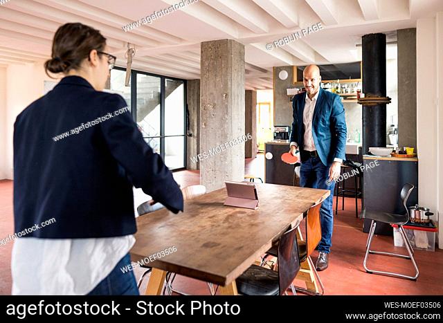 Man and woman playing while standing by table at cafeteria in office