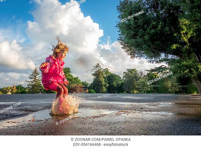 Little Caucasian girl jumping into the puddle after rain in english countryside