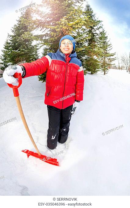 Arabian boy with shovel in winter during day near fir trees in countryhouse