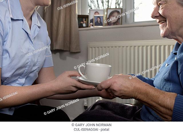 Personal care assistant handing senior woman cup of tea