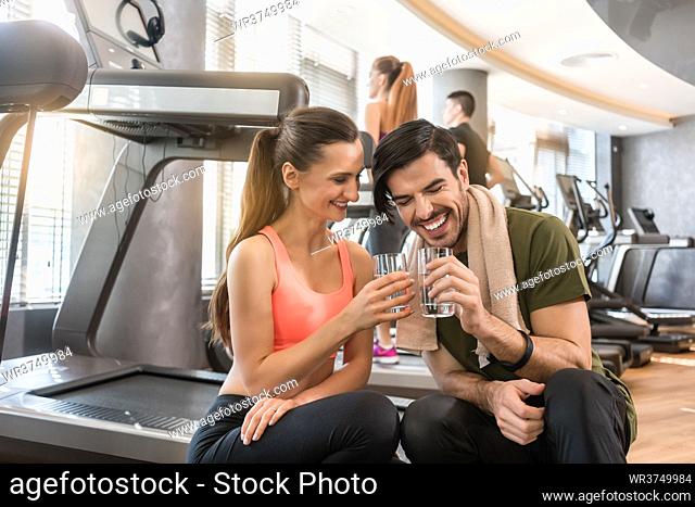 Cheerful young man and woman with a healthy lifestyle drinking plain water for hydration during break at the fitness club