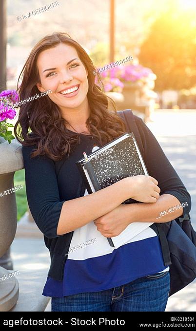 Portrait of pretty young female student carrying books on school campus