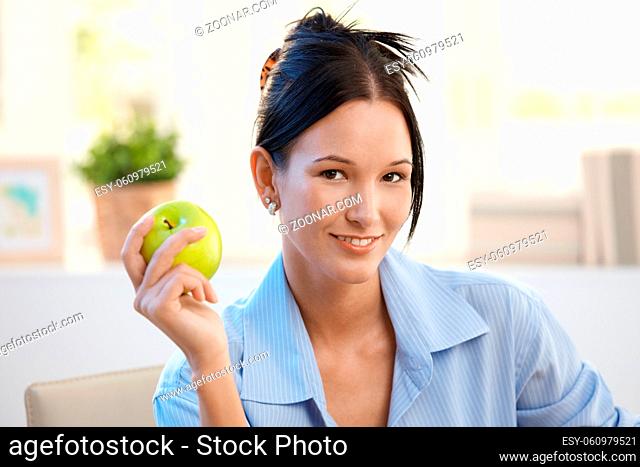 Smiling young woman posing with green apple, looking at camera