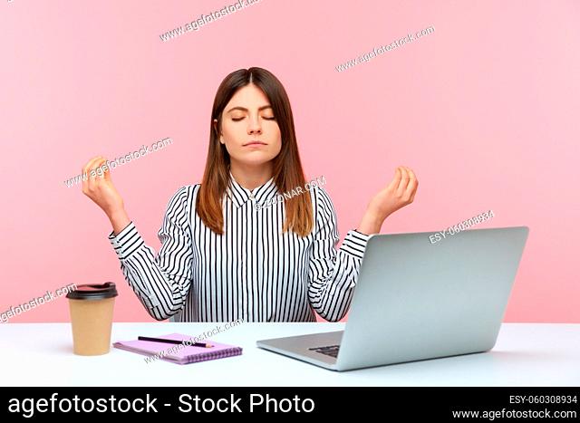 Calm concentrated business woman in striped shirt meditating sitting workplace at home office, resting and relaxing, looking for inspiration
