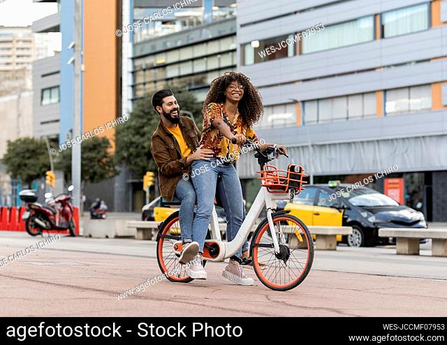 Happy boyfriend enjoying with girlfriend riding bicycle at footpath
