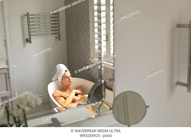 Thoughtful woman sitting in the bathtub and looking at the window in bathroom at home