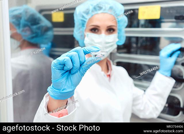 Doctor or scientist showing dish with egg cells in front of incubator