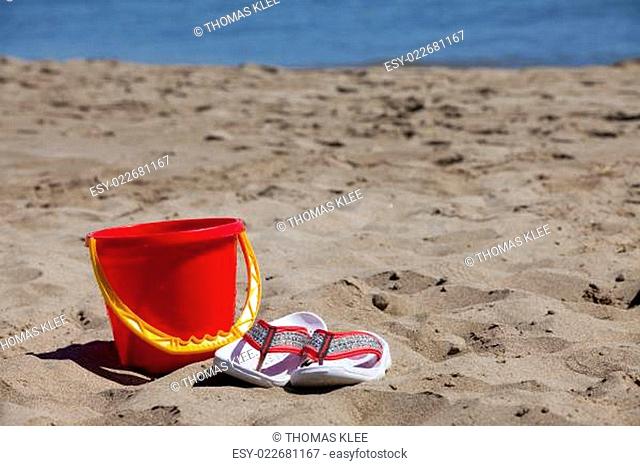 Flip Flops und ein roter Eimer am Strand