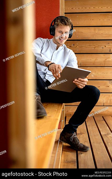 Smiling man wearing headphones using digital tablet while sitting at home