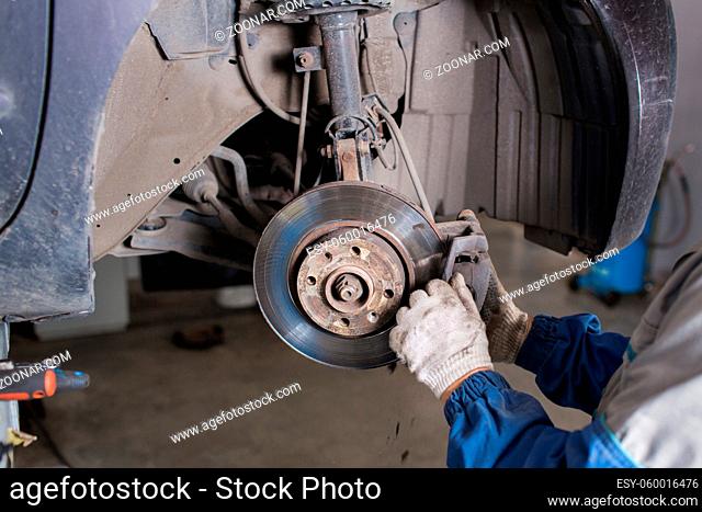 Brand new brake disc on car in a garage. Auto mechanic repairing a car