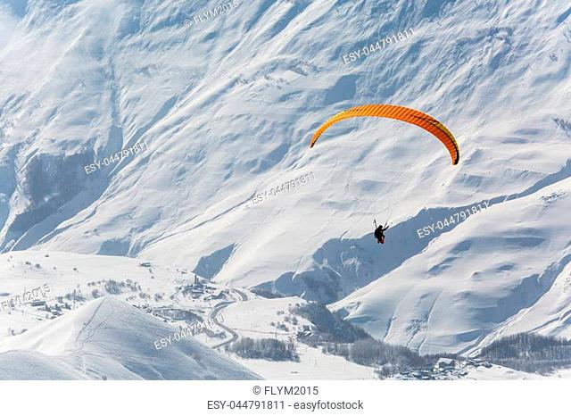 Parachute sky-diver flying in clouds above mountains with fresh snow on Sunny winter day in the ski resort. Travel adventure concept. space for text